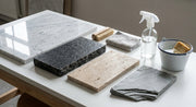 Verschiedene Naturstein-Musterplatten und Reinigungsutensilien geordnet auf einer hellen Werkbank